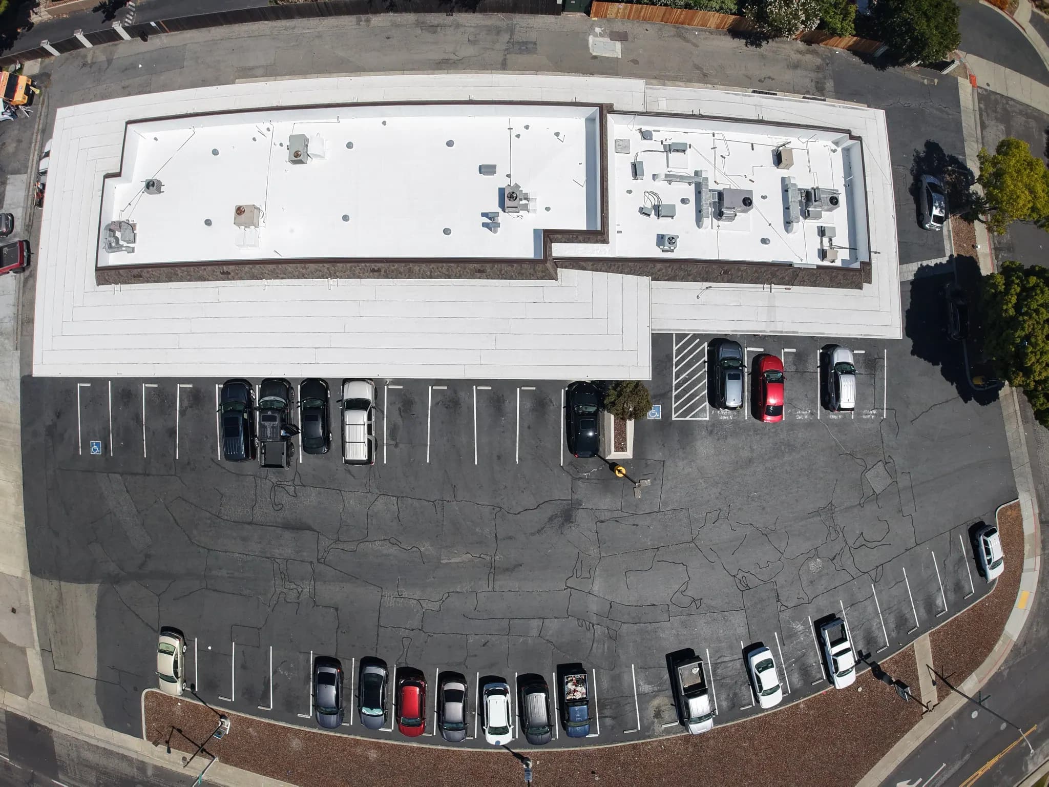 Straight-down drone view of a strip center’s white roof and its parking lot
