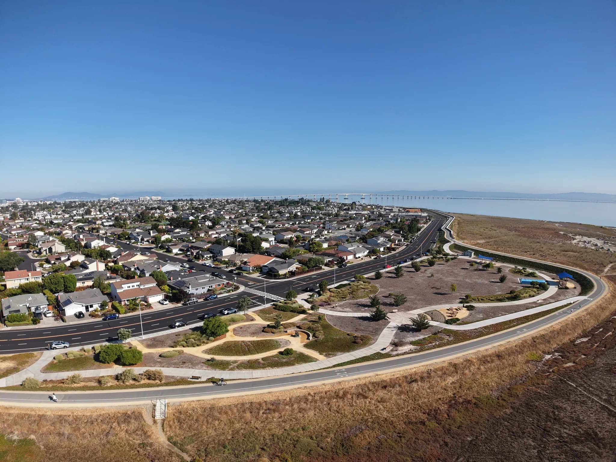 Wide drone view over a waterfront neighborhood, a shoreline path and the bay