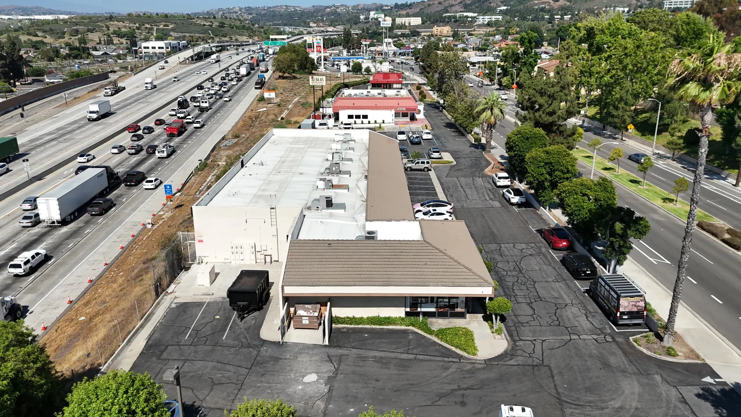 Aerial view of a single-story retail center and its parking lot beside a freeway