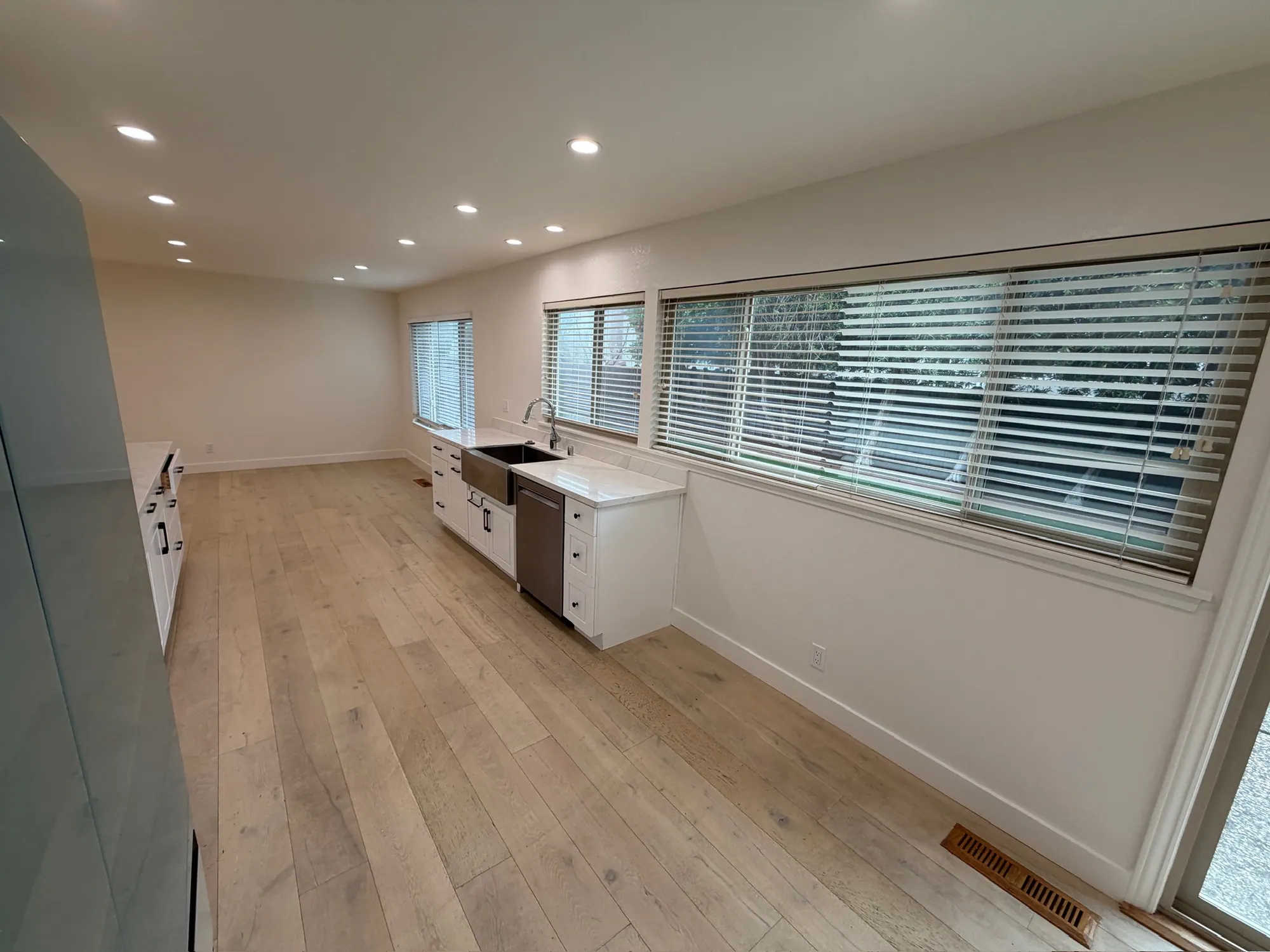 New kitchen along a wall of windows, with white cabinets and plank floor
