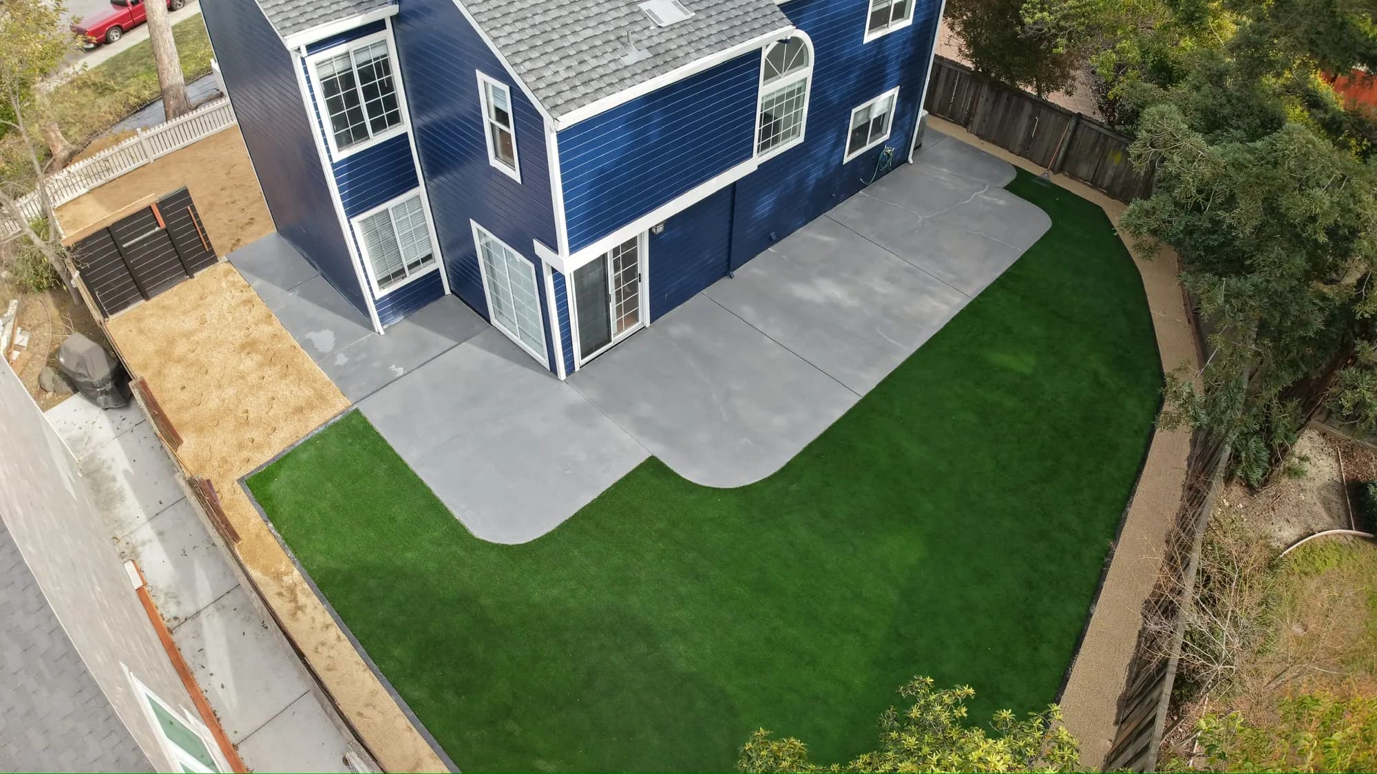 Drone view of a navy two-story home, new turf and a curved concrete patio
