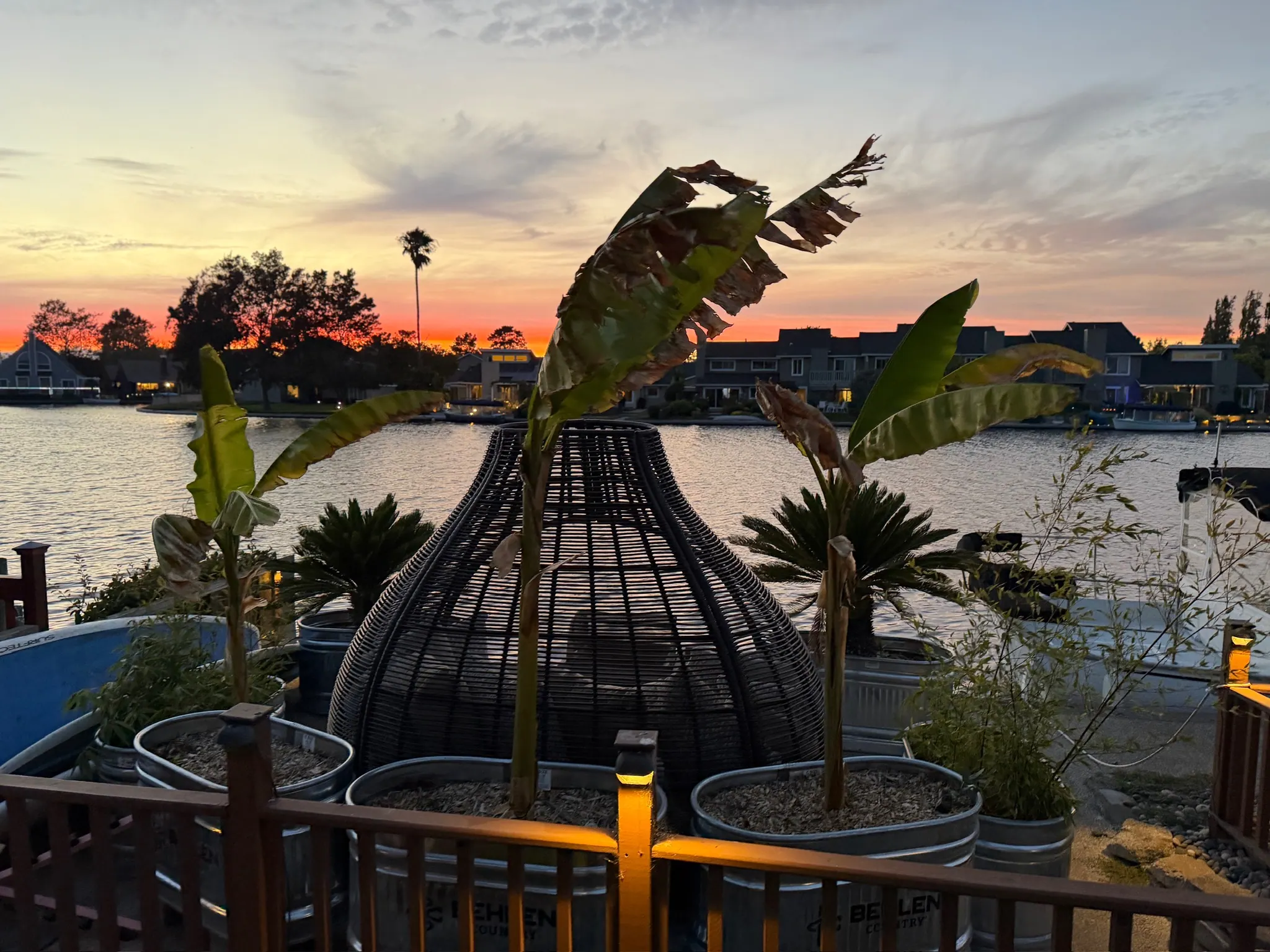 Waterfront deck at sunset with a woven lounge pod and potted palms