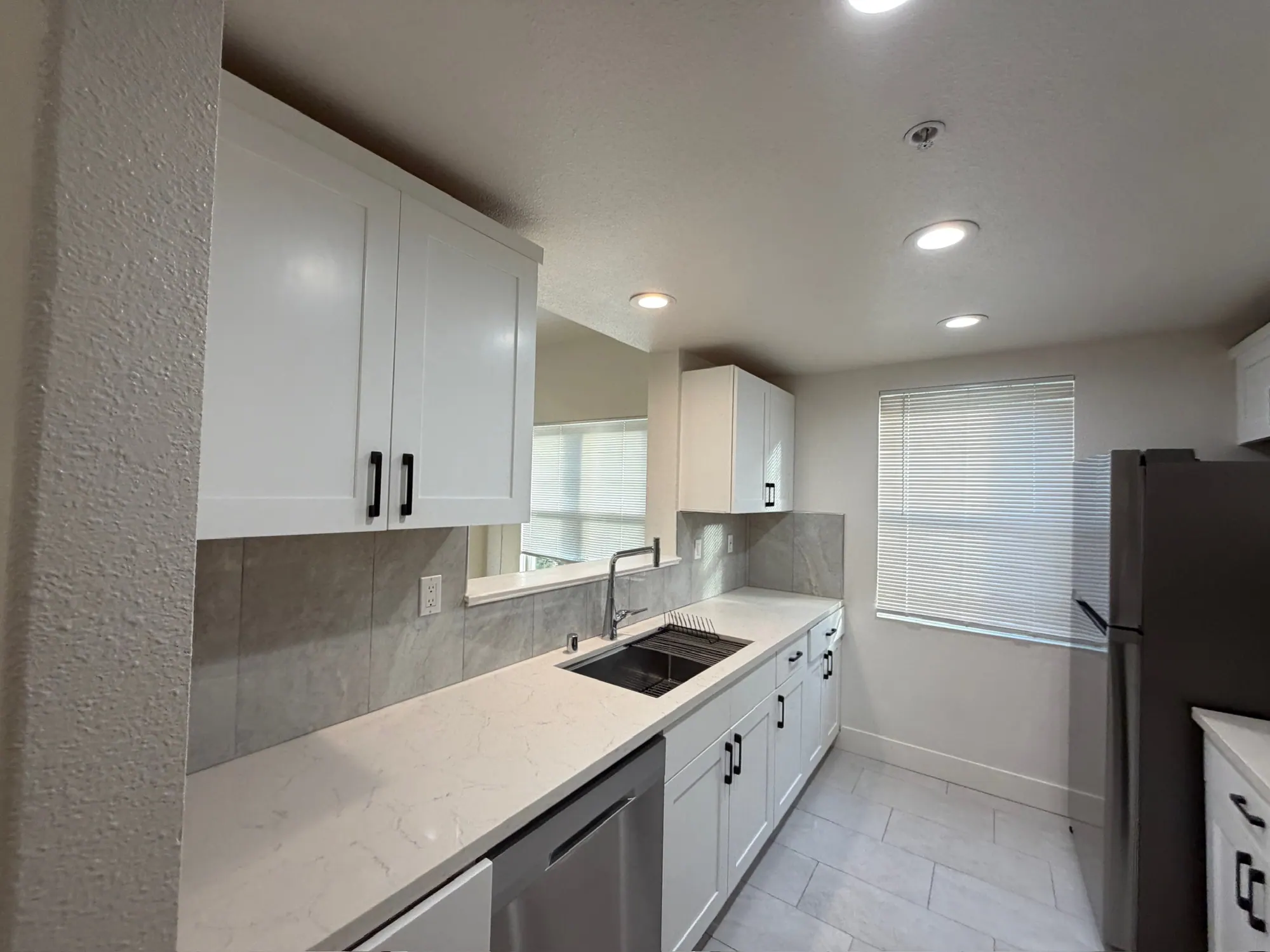 Condo kitchen with white shaker cabinets, quartz counters and a tiled floor, ready for rent