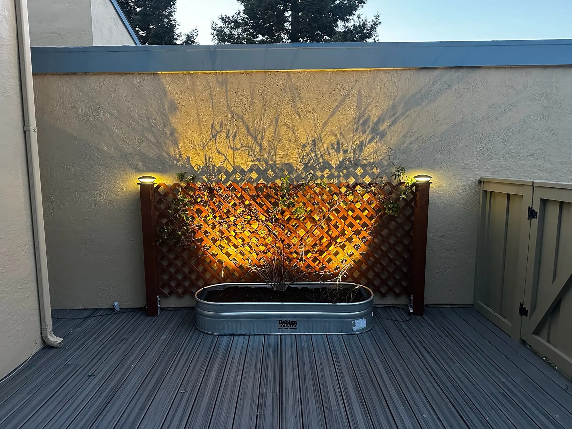 Rear patio at dusk: an uplit lattice wall, a stock-tank planter and new decking