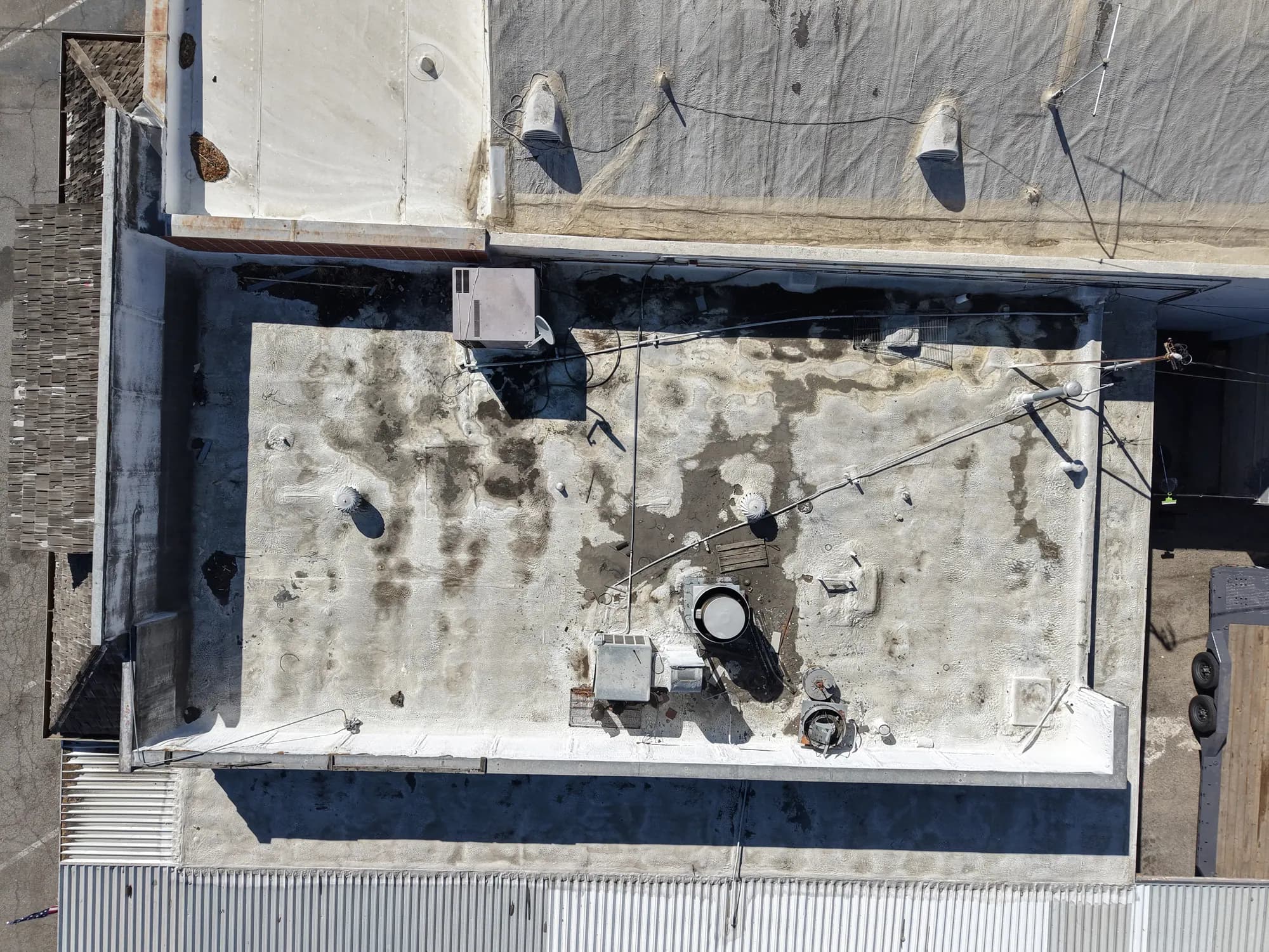 Close drone survey of a flat commercial roof showing weathering, vents and a rooftop unit