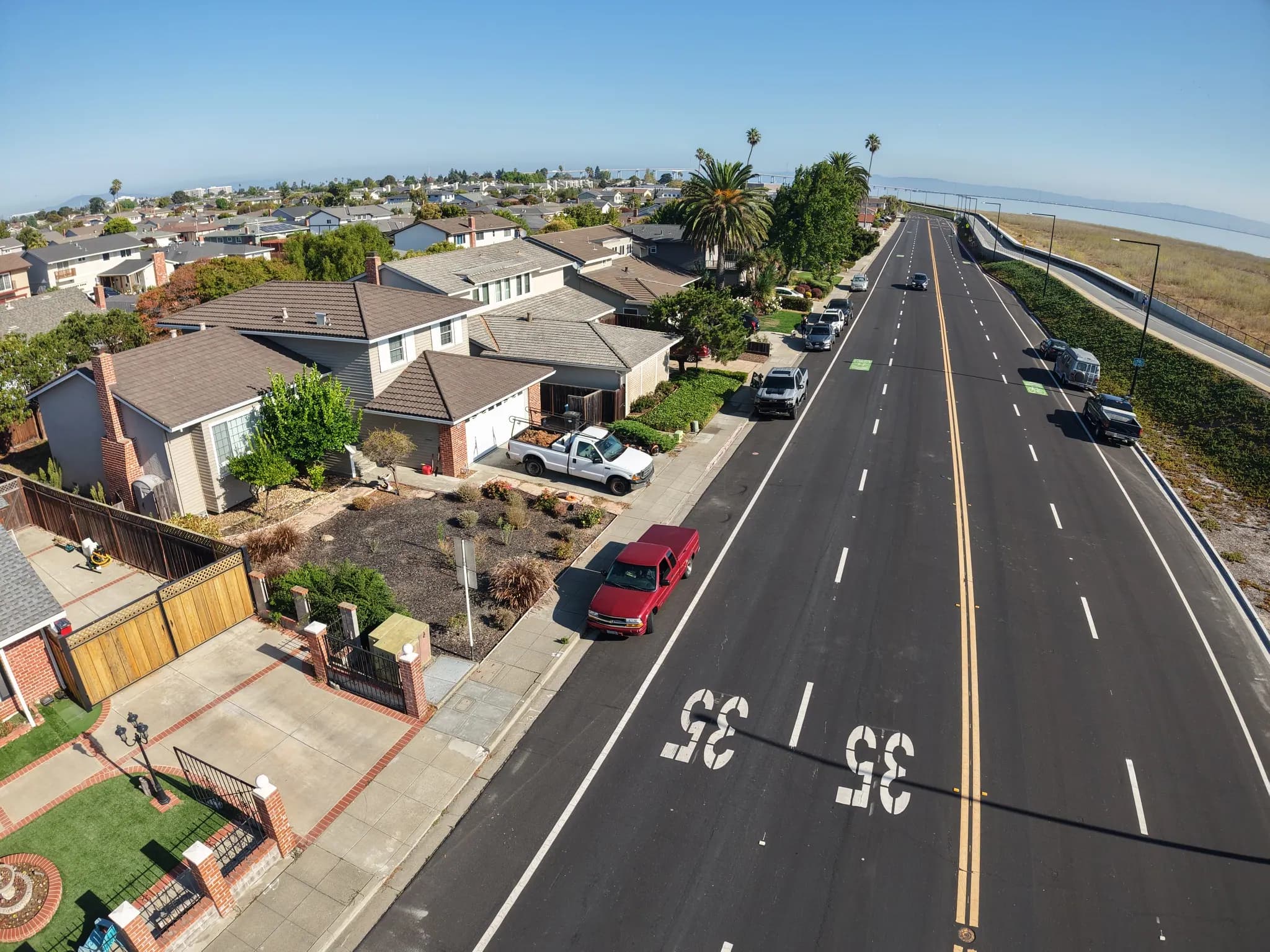 Drone view along a boulevard lined with tile-roofed homes toward the water