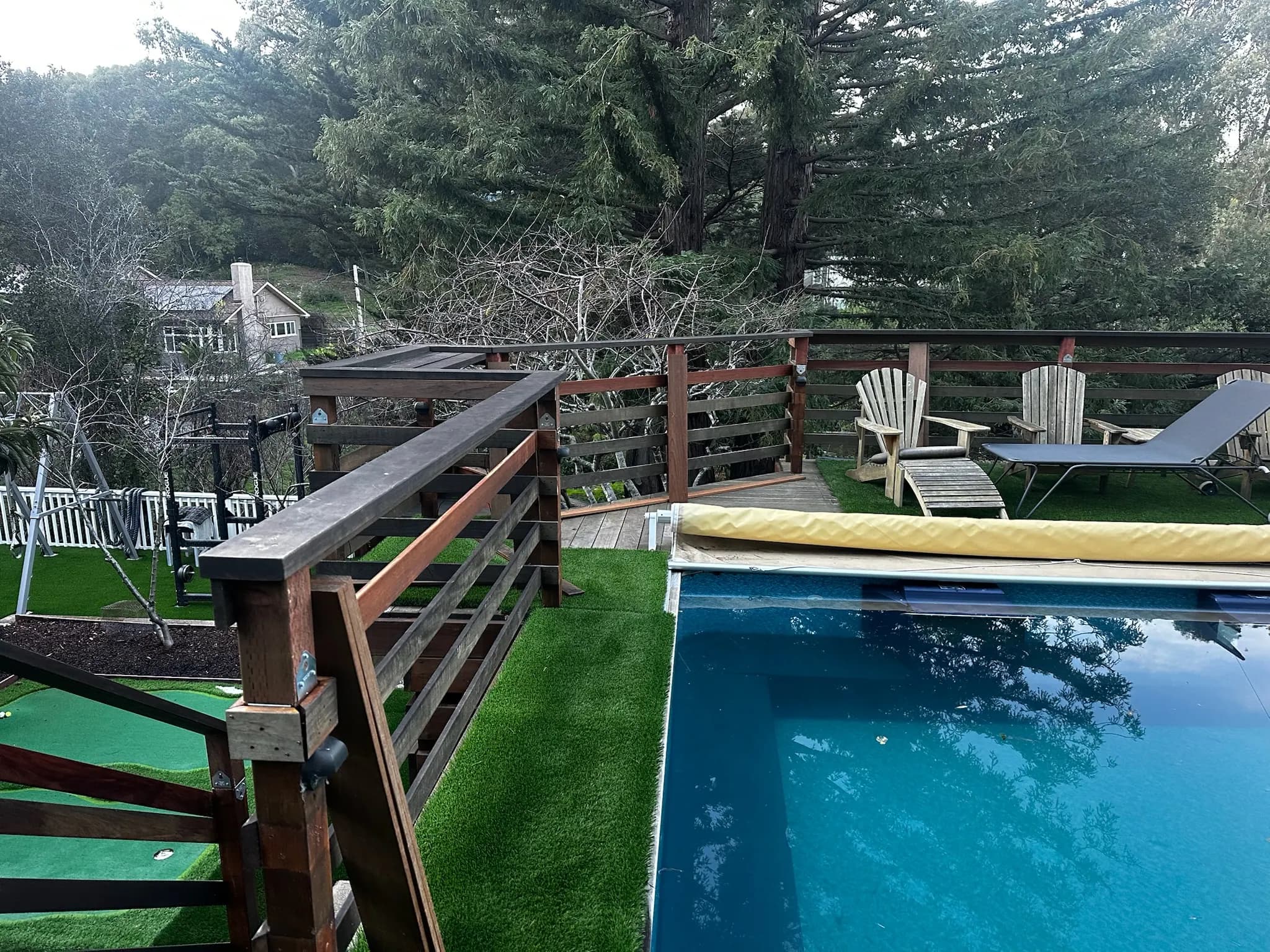 Pool with turf surround, wood railing and deck chairs under tall redwoods