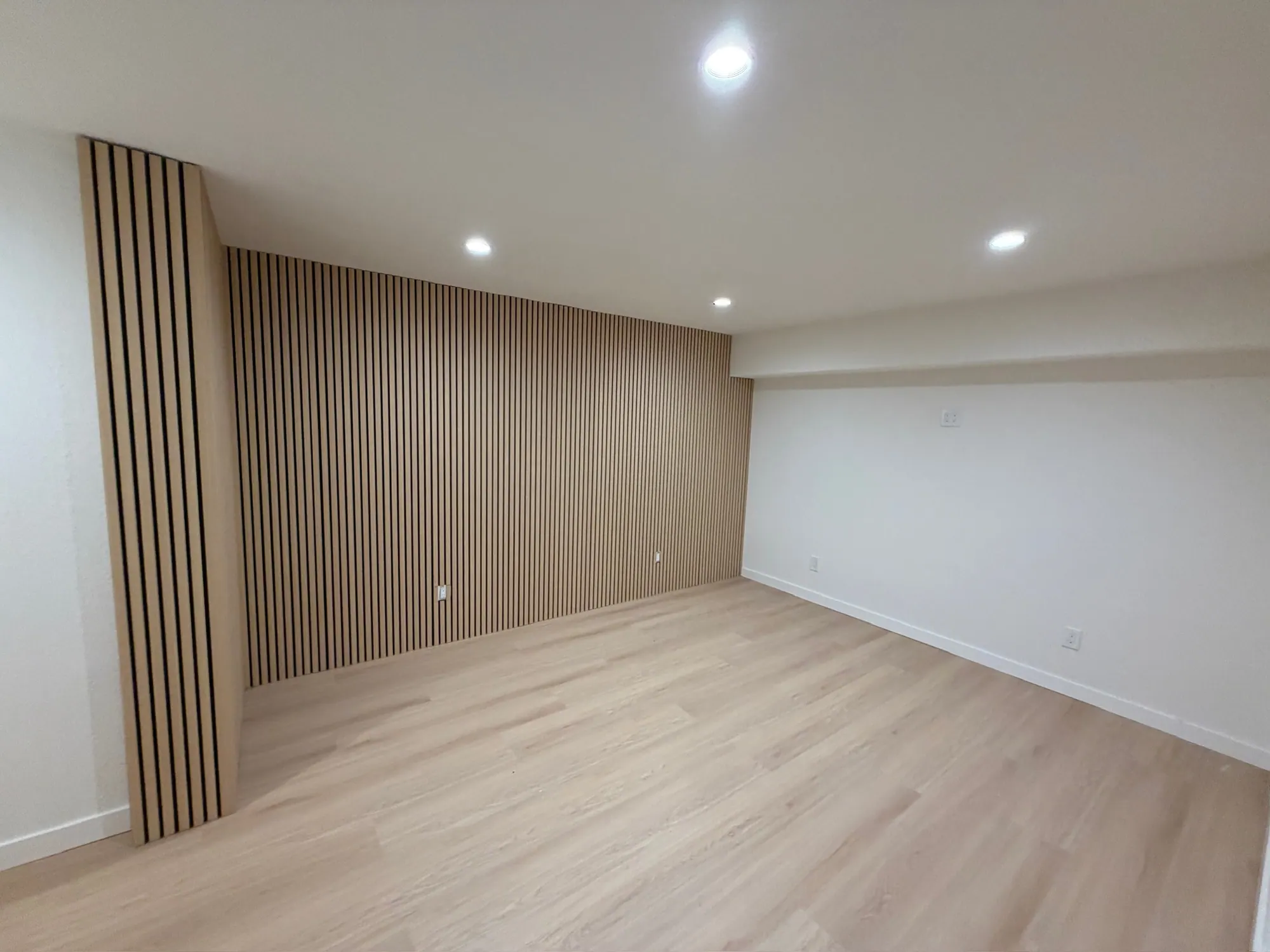 Finished room with a floor-to-ceiling wood slat accent wall, recessed lights and new plank floor