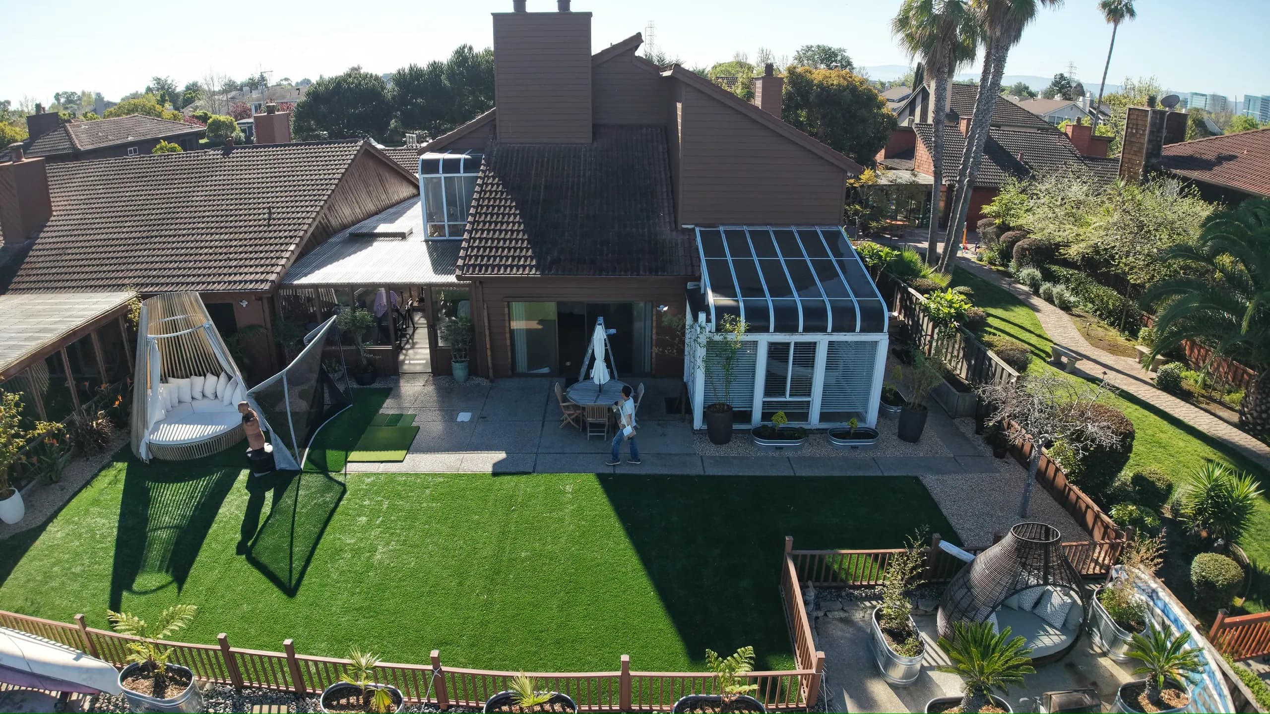 Drone view of the house, its glass sunroom and the lawn and planting beds