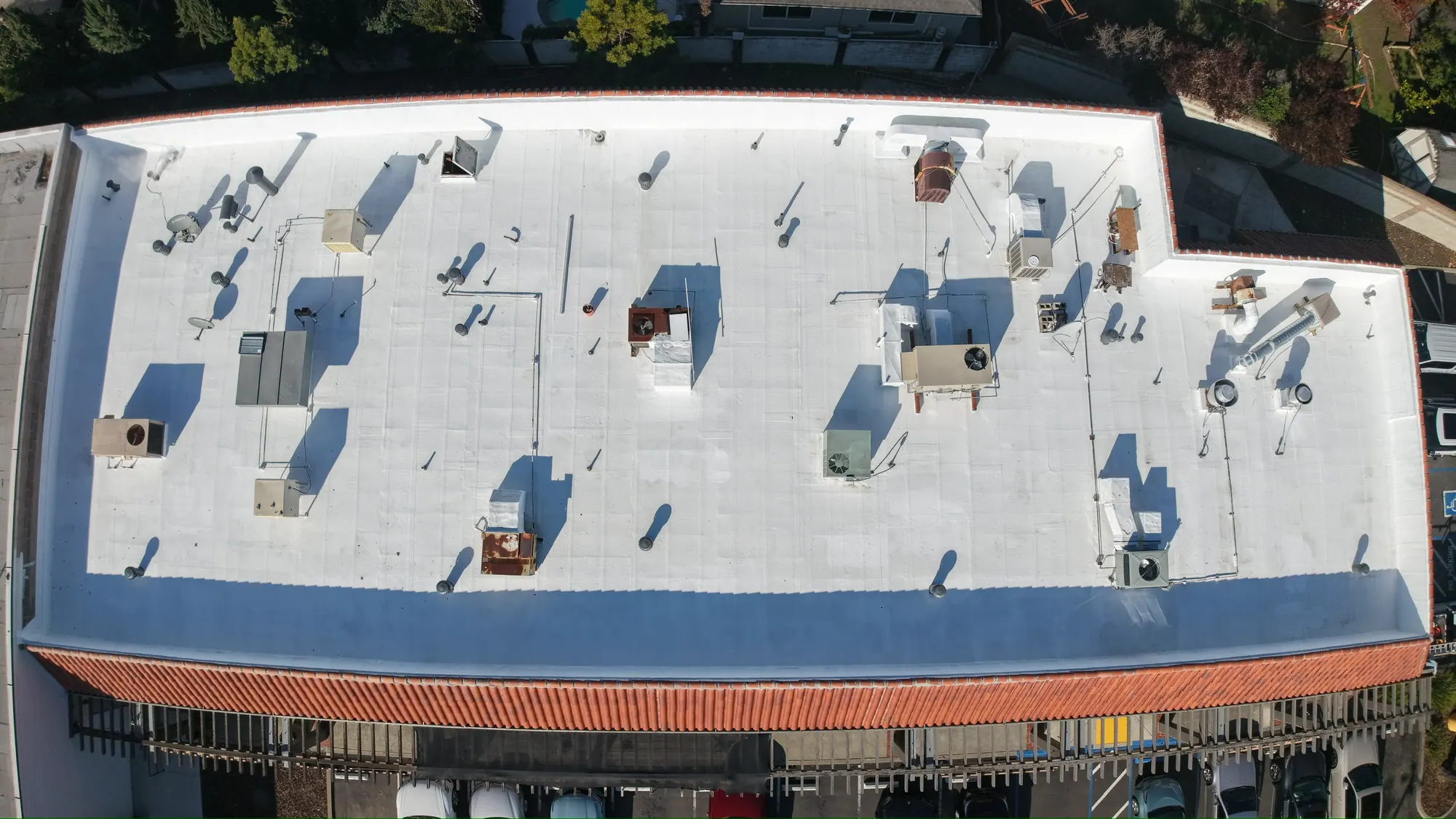 Freshly coated white roof and rooftop units above a red tile mansard